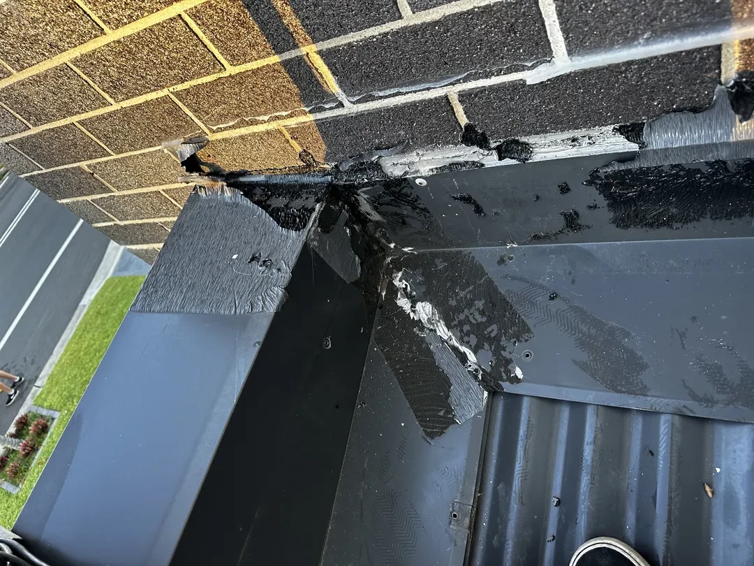 Damaged flashing on rooftop near brick wall corner.